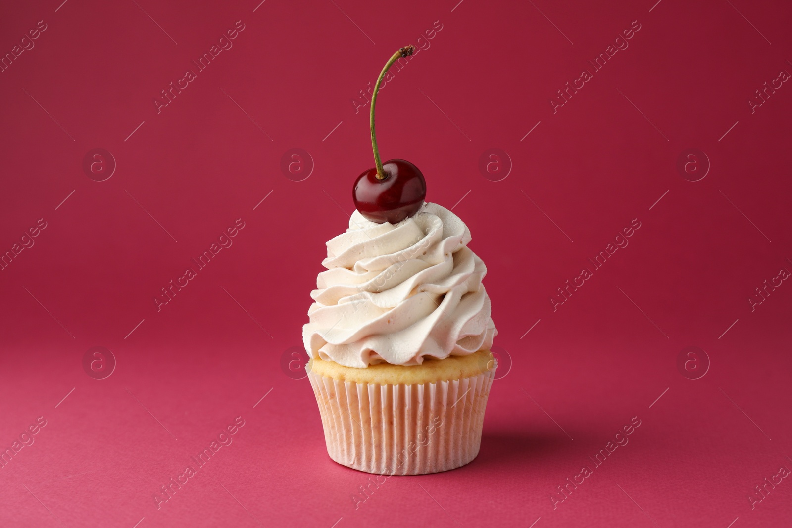 Photo of Delicious cupcake with cream and cherry on red background