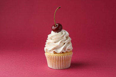 Delicious cupcake with cream and cherry on red background