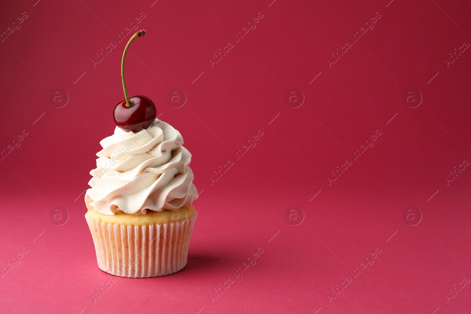 Photo of Delicious cupcake with cream and cherry on red background, space for text