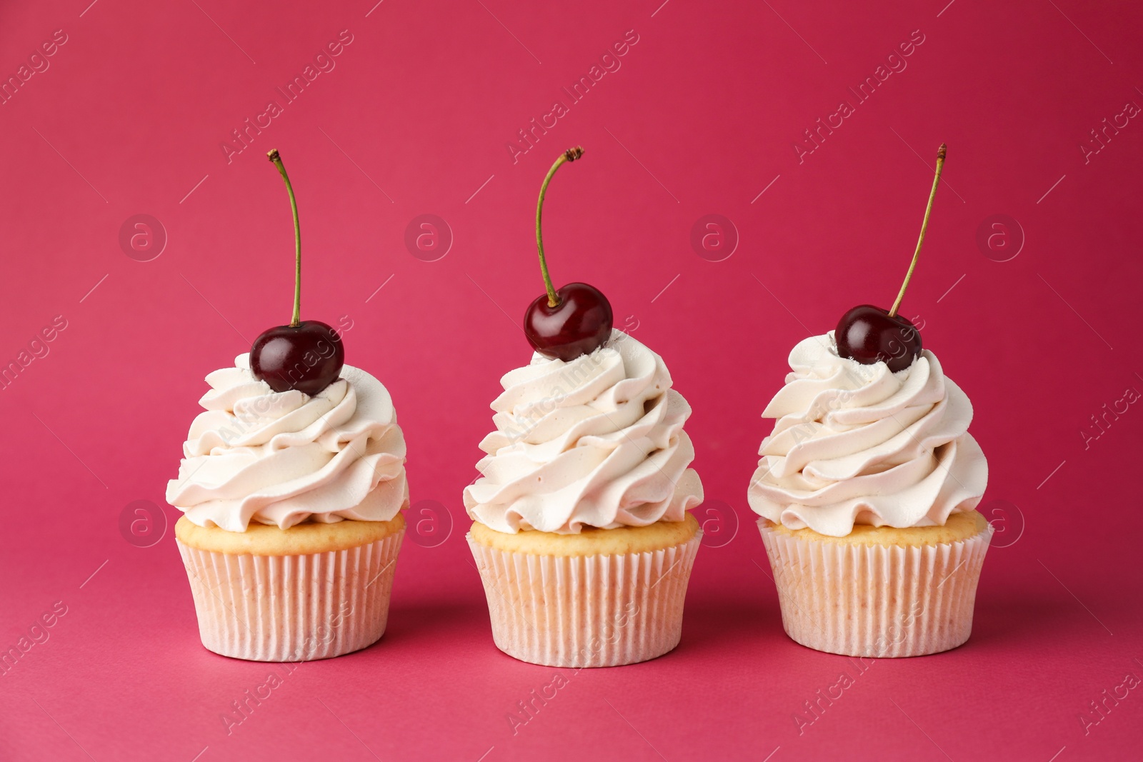 Photo of Delicious cupcakes with cream and cherries on red background