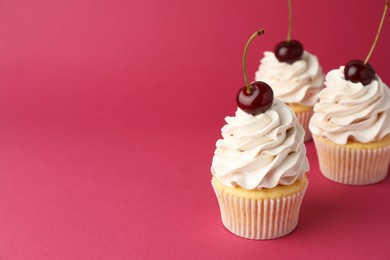 Delicious cupcakes with cream and cherries on red background, space for text