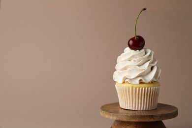 Photo of Delicious cupcake with cream and cherry on dark beige background, space for text