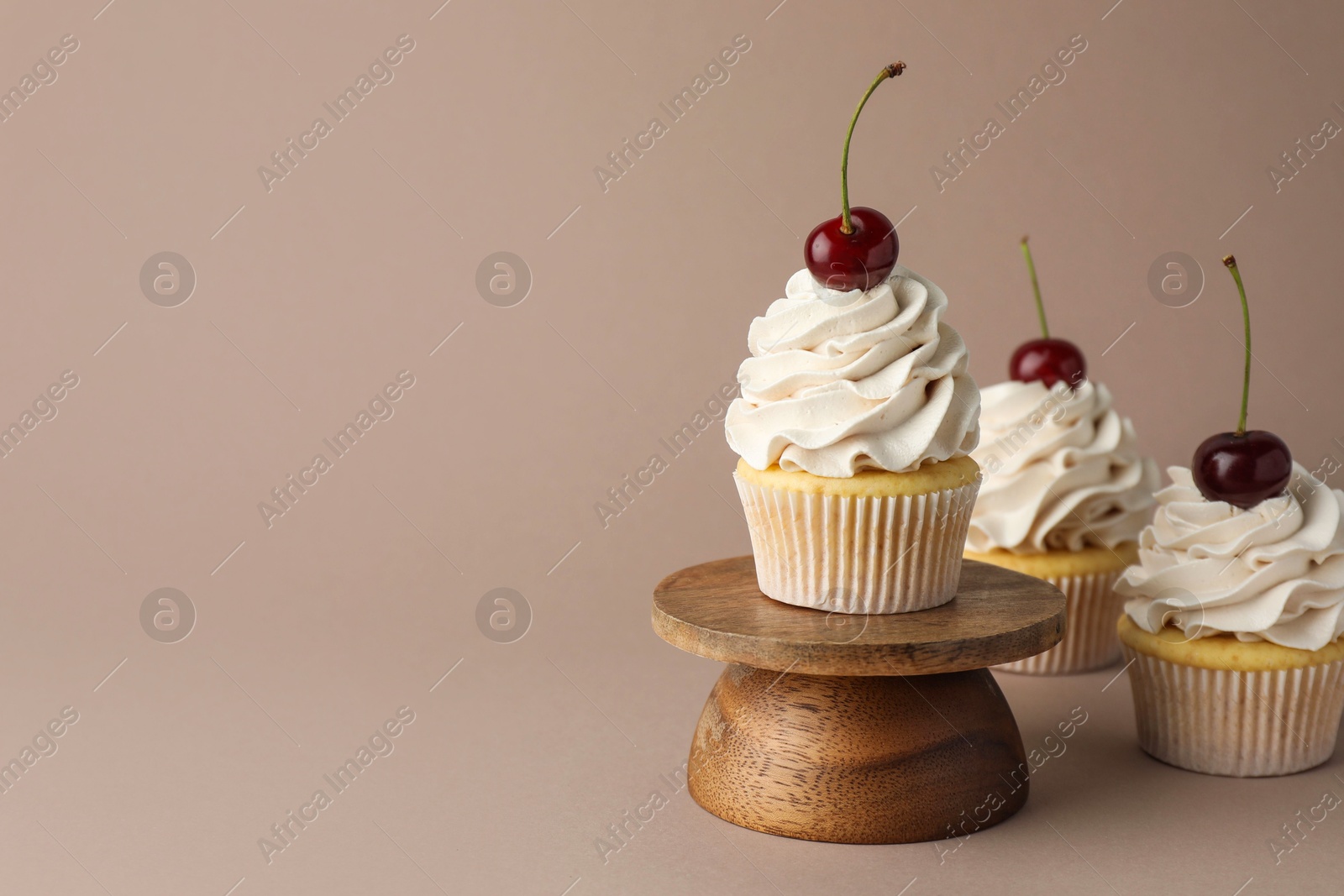 Photo of Delicious cupcakes with cream and cherries on dark beige background, space for text