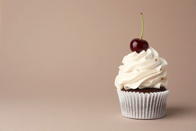 Photo of Delicious cupcake with cream and cherry on dark beige background, space for text