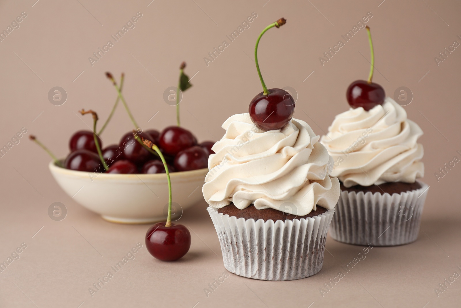 Photo of Delicious cupcakes with cream and cherries on dark beige background