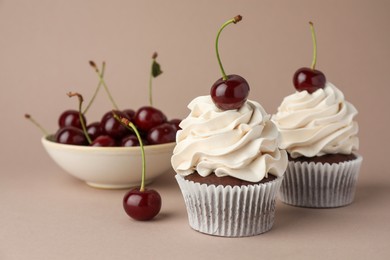 Photo of Delicious cupcakes with cream and cherries on dark beige background