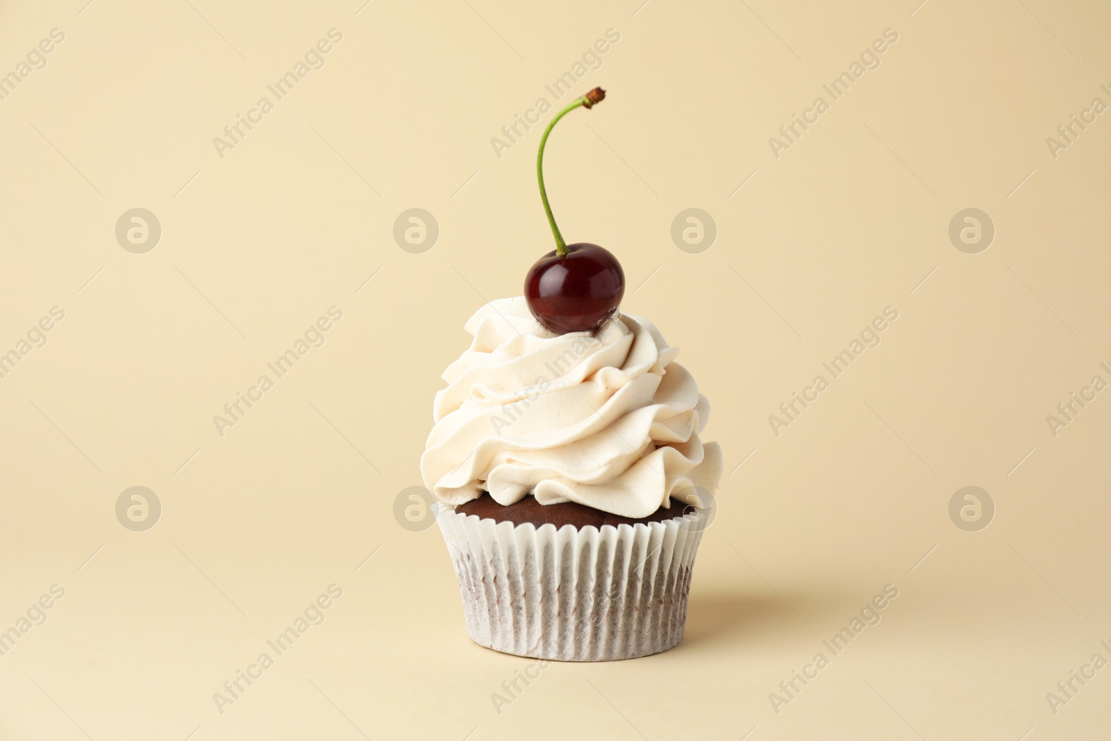 Photo of Delicious cupcake with cream and cherry on beige background