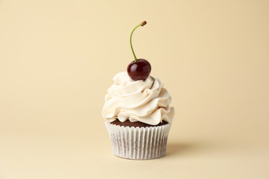 Photo of Delicious cupcake with cream and cherry on beige background