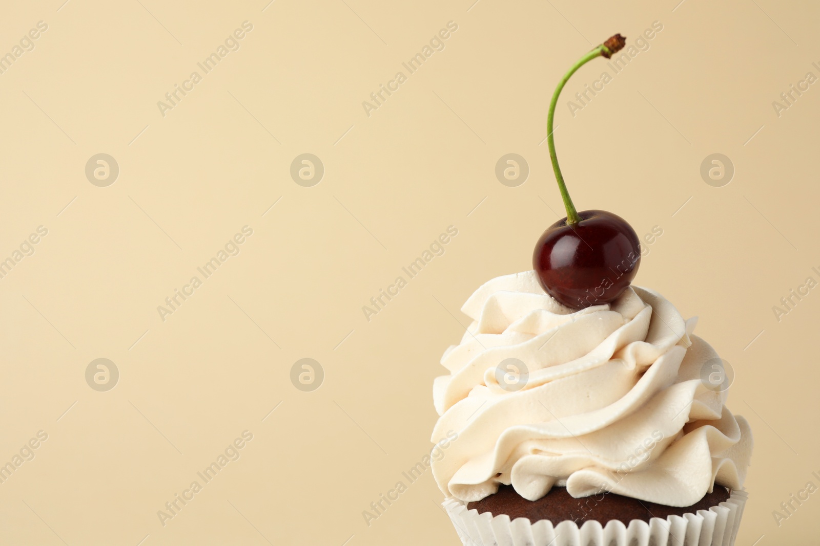 Photo of Delicious cupcake with cream and cherry on beige background, space for text