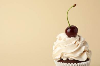 Delicious cupcake with cream and cherry on beige background, space for text