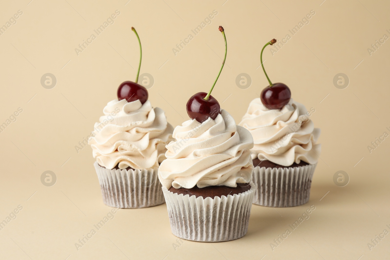 Photo of Delicious cupcakes with cream and cherries on beige background