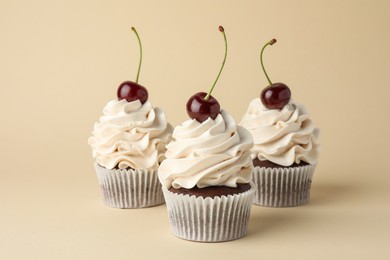 Delicious cupcakes with cream and cherries on beige background