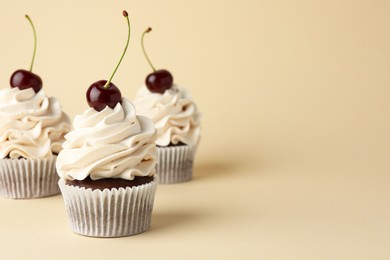 Delicious cupcakes with cream and cherries on beige background, space for text