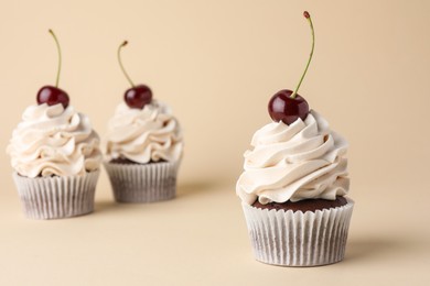 Photo of Delicious cupcakes with cream and cherries on beige background