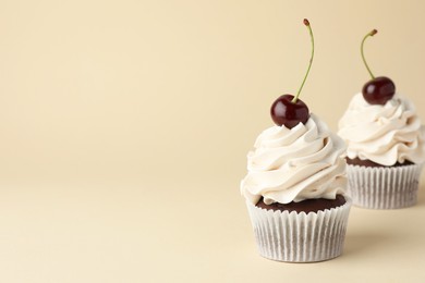 Delicious cupcakes with cream and cherries on beige background, space for text