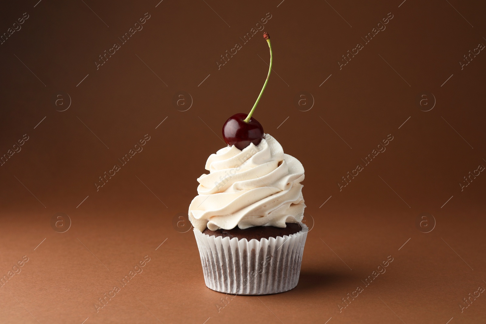 Photo of Delicious cupcake with cream and cherry on brown background