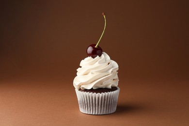 Photo of Delicious cupcake with cream and cherry on brown background