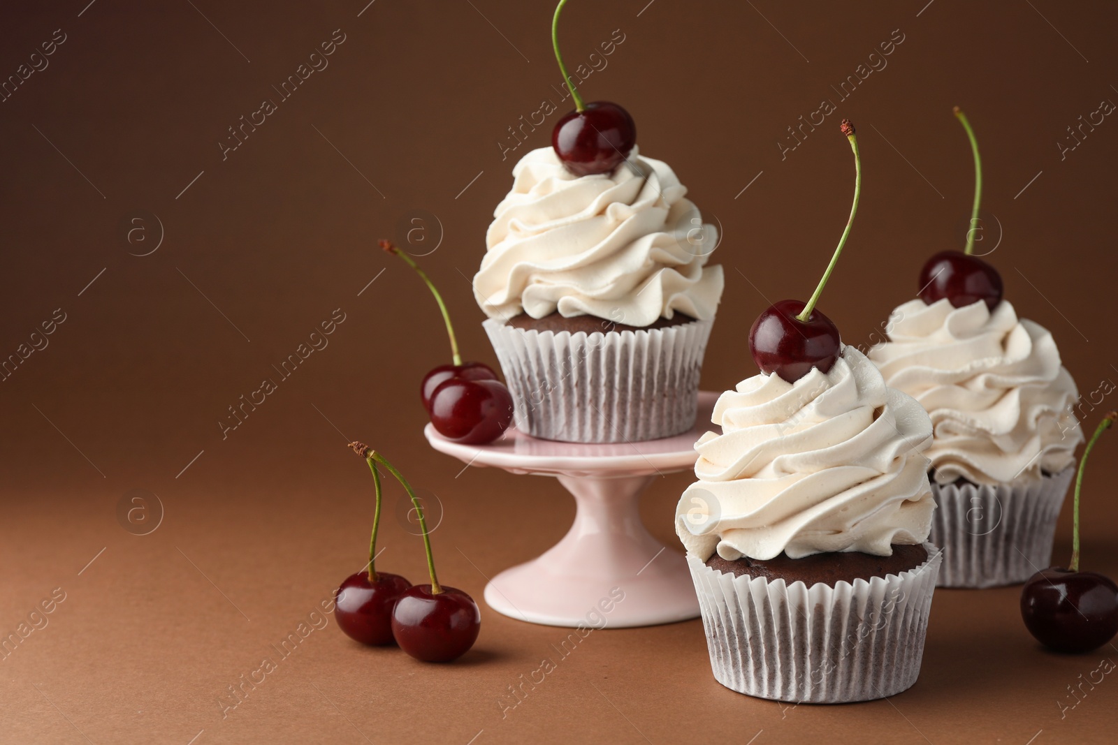 Photo of Delicious cupcakes with cream and cherries on brown background, space for text