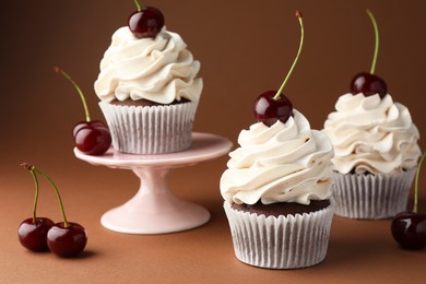 Photo of Delicious cupcakes with cream and cherries on brown background