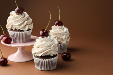 Delicious cupcakes with cream and cherries on brown background, space for text