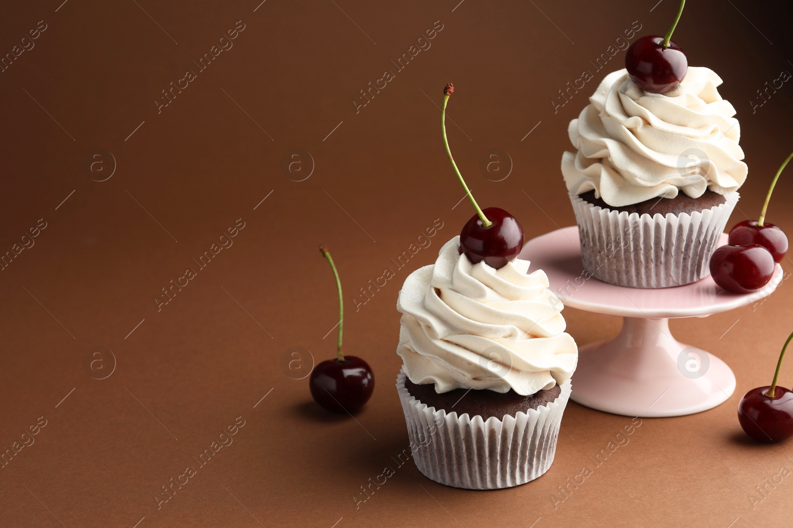 Photo of Delicious cupcakes with cream and cherries on brown background, space for text