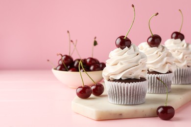 Photo of Delicious cupcakes with cream and cherries on pink table, space for text