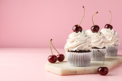 Photo of Delicious cupcakes with cream and cherries on pink table, space for text