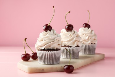 Photo of Delicious cupcakes with cream and cherries on pink table