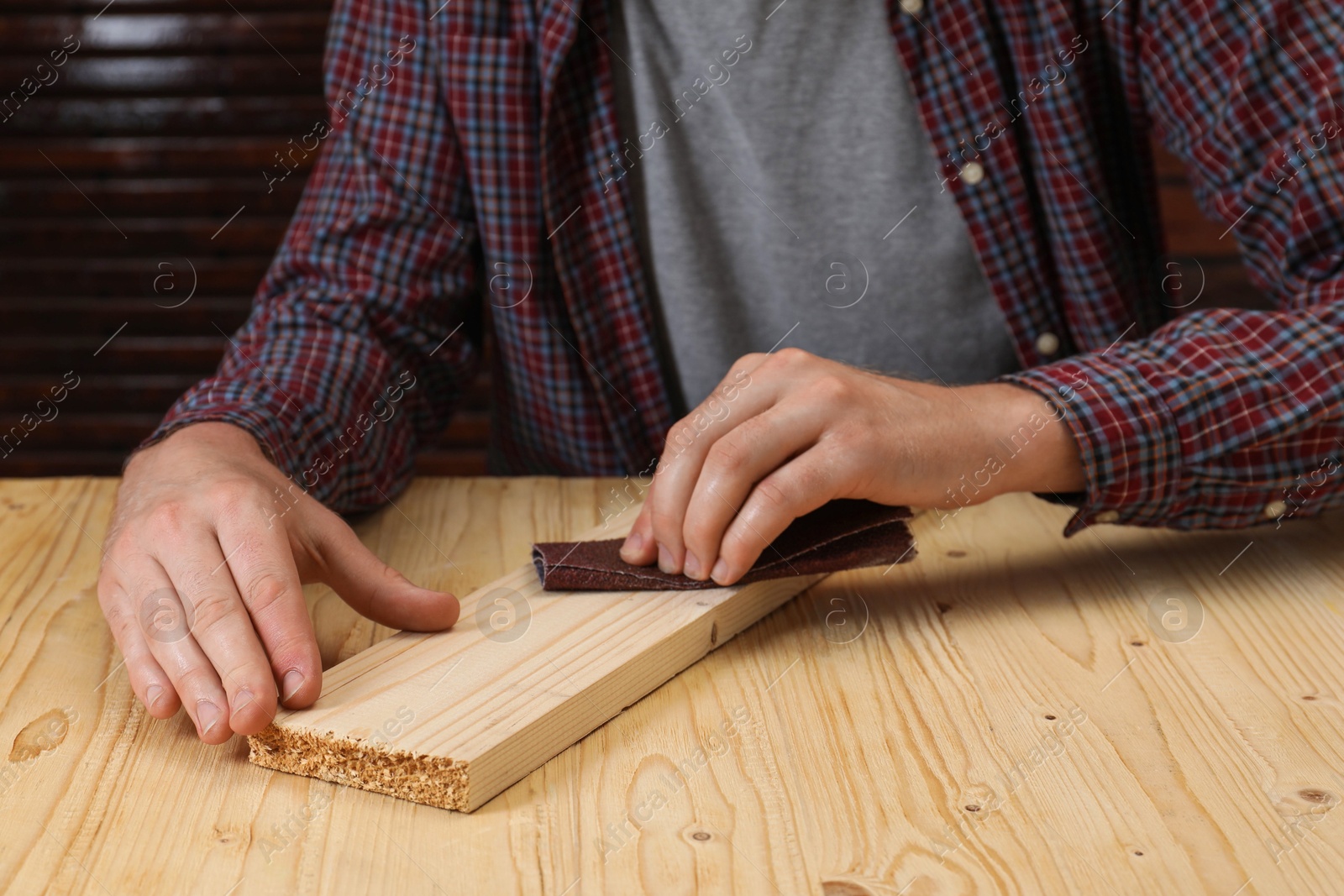 Photo of Man polishing wooden plank with sandpaper at table, closeup