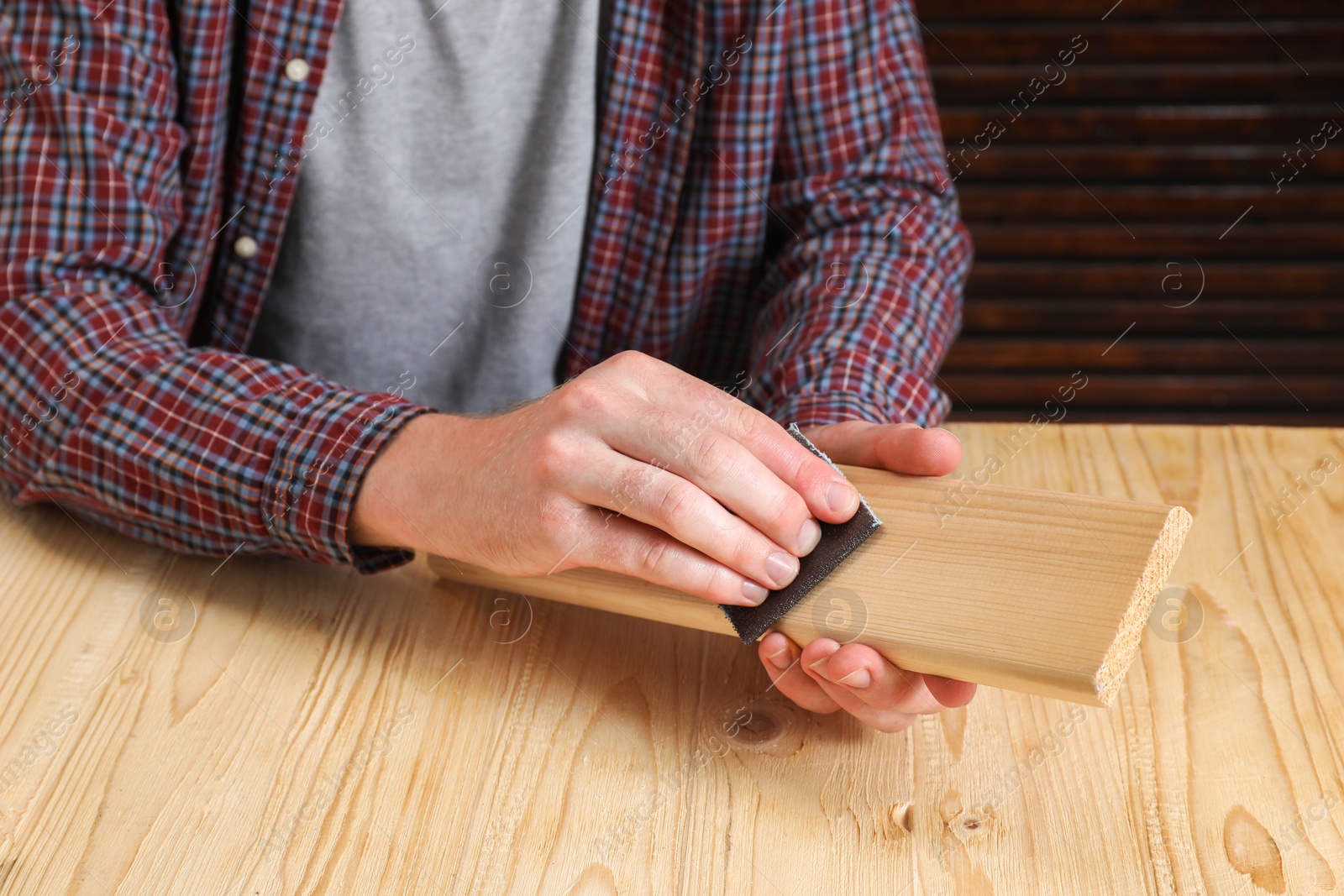 Photo of Man polishing wooden plank with sandpaper at table, closeup