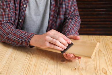 Man polishing wooden plank with sandpaper at table, closeup