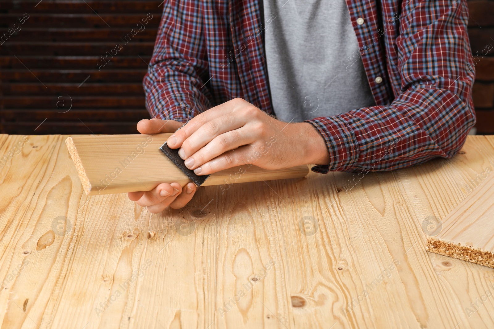 Photo of Man polishing wooden plank with sandpaper at table, closeup