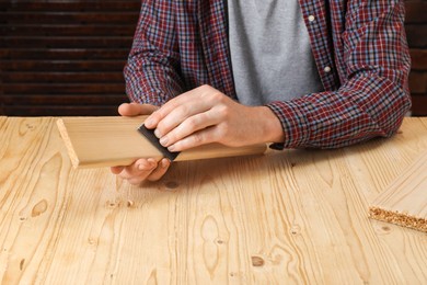 Man polishing wooden plank with sandpaper at table, closeup