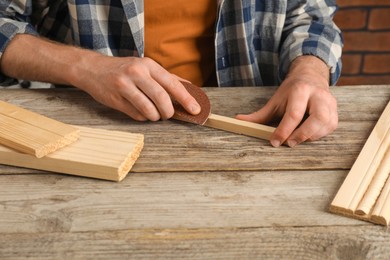 Photo of Man polishing wooden plank with sandpaper at table, closeup