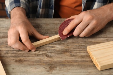 Photo of Man polishing wooden plank with sandpaper at table, closeup