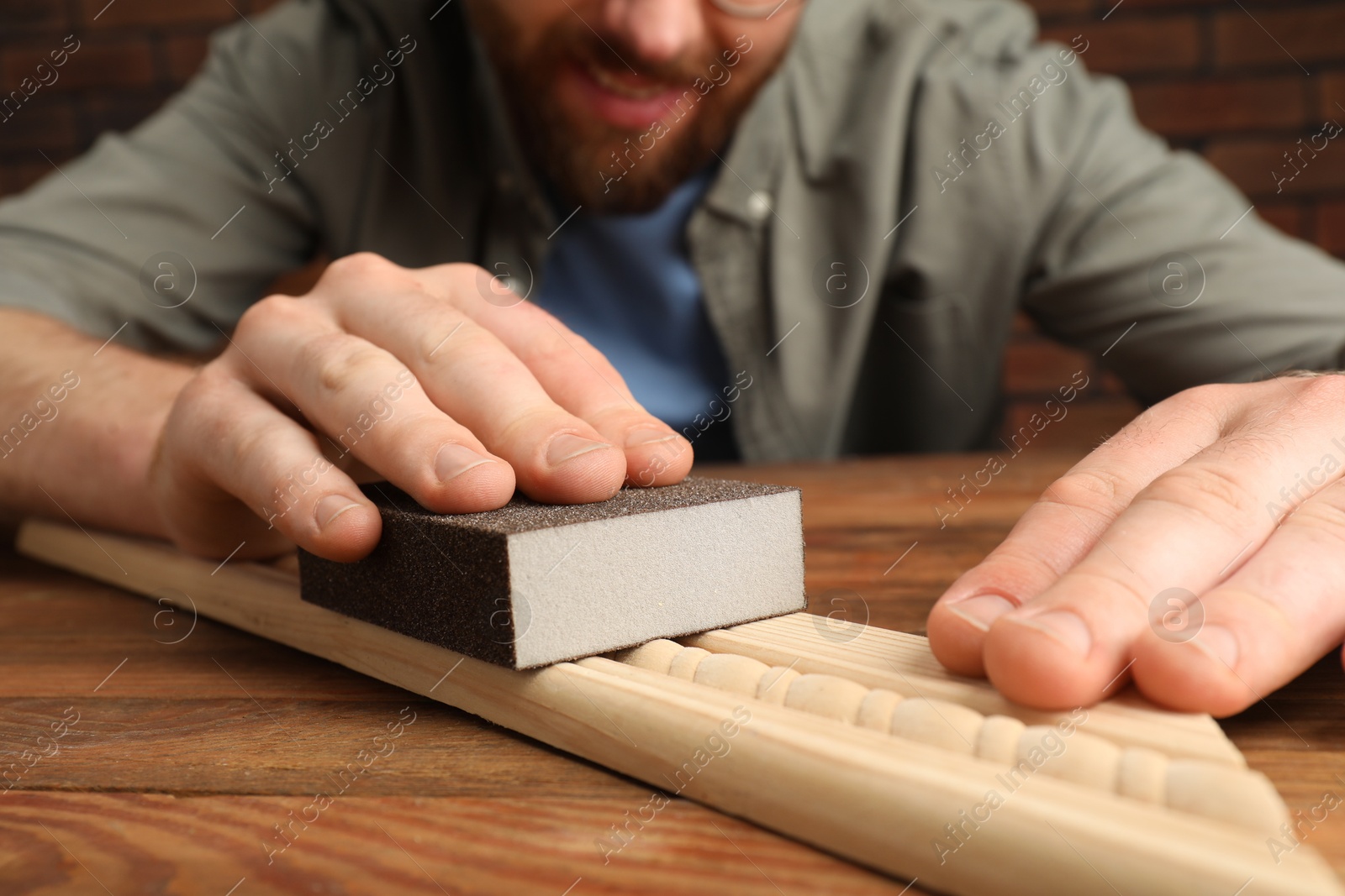 Photo of Man polishing wooden plank with sandpaper at table, closeup