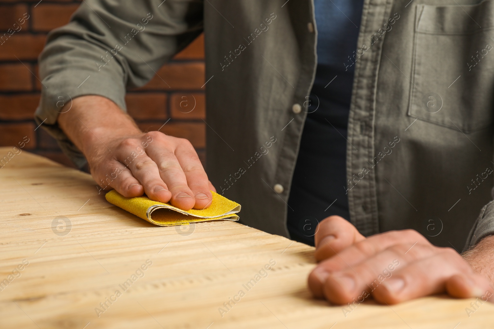 Photo of Man polishing wooden plank with sandpaper at table, closeup