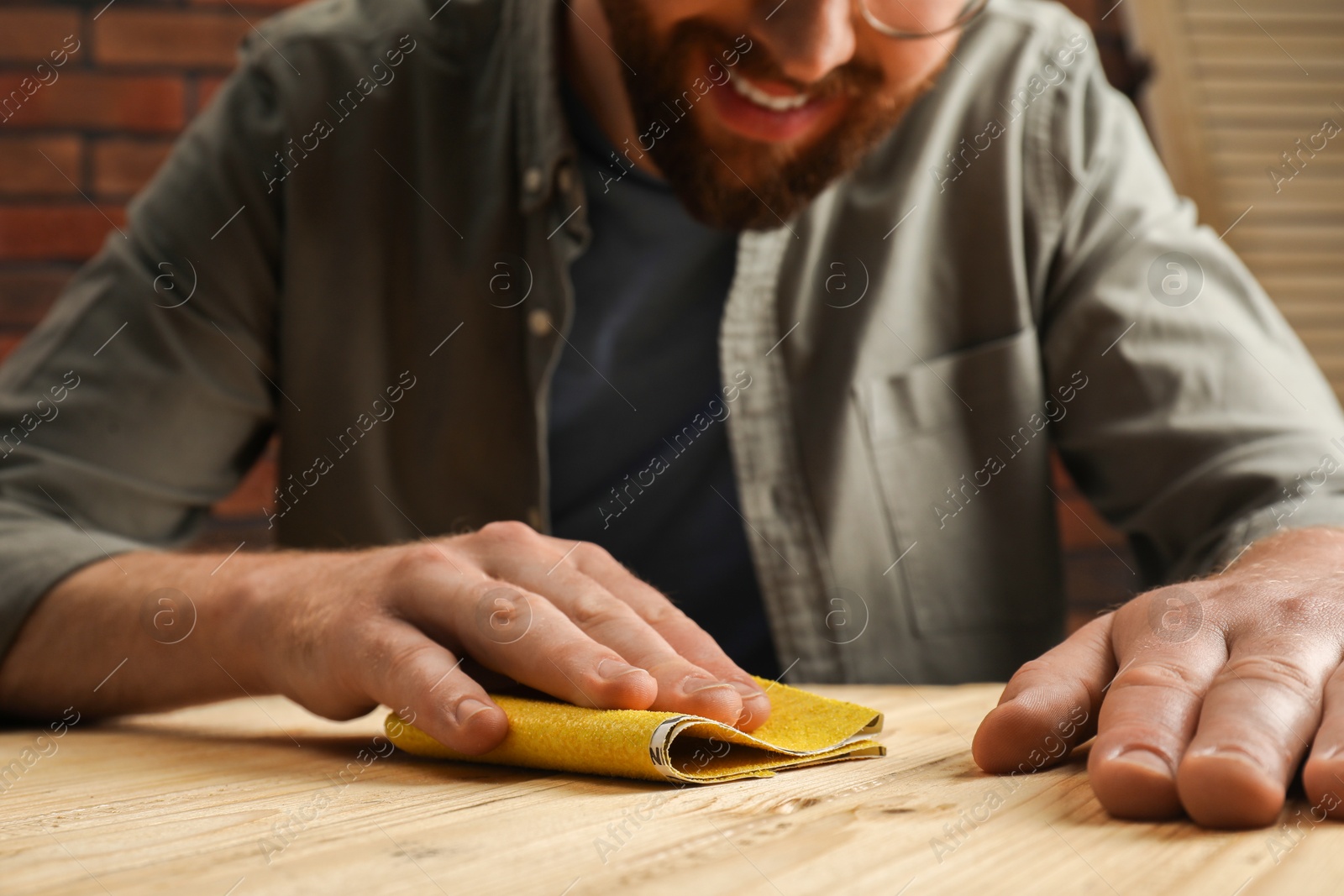 Photo of Man polishing wooden plank with sandpaper at table, closeup