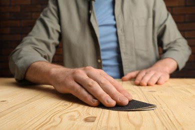 Photo of Man polishing wooden plank with sandpaper at table, closeup