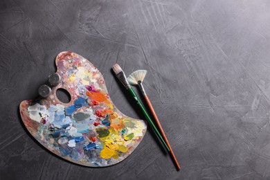 Photo of Artist's palette, brushes and paints on grey table, flat lay. Space for text