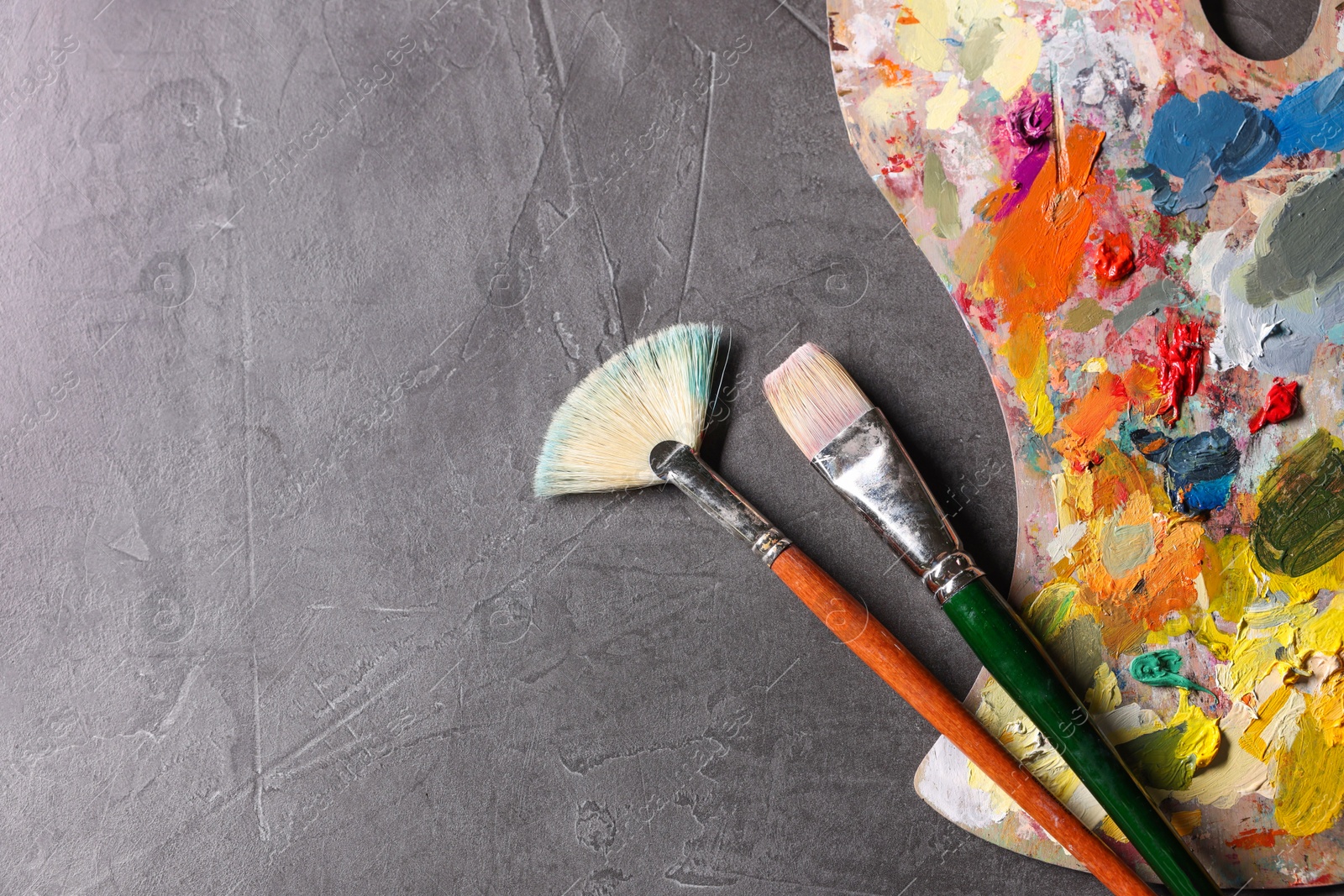 Photo of Artist's palette, brushes and paints on grey table, flat lay. Space for text