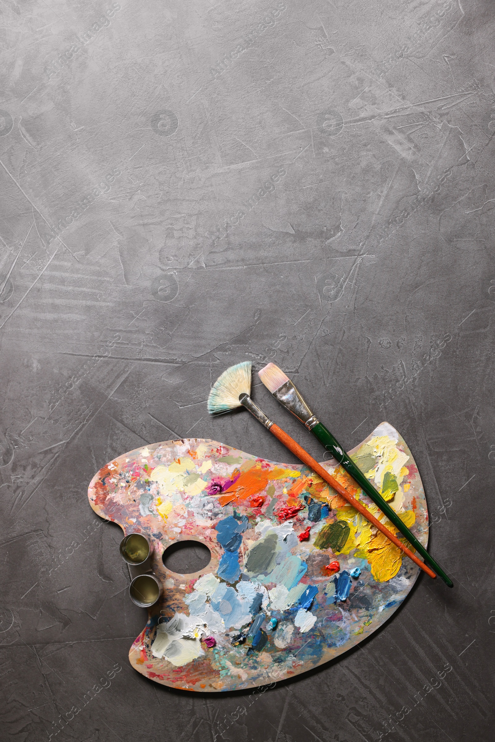 Photo of Artist's palette, brushes and paints on grey table, flat lay. Space for text