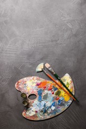 Photo of Artist's palette, brushes and paints on grey table, flat lay. Space for text