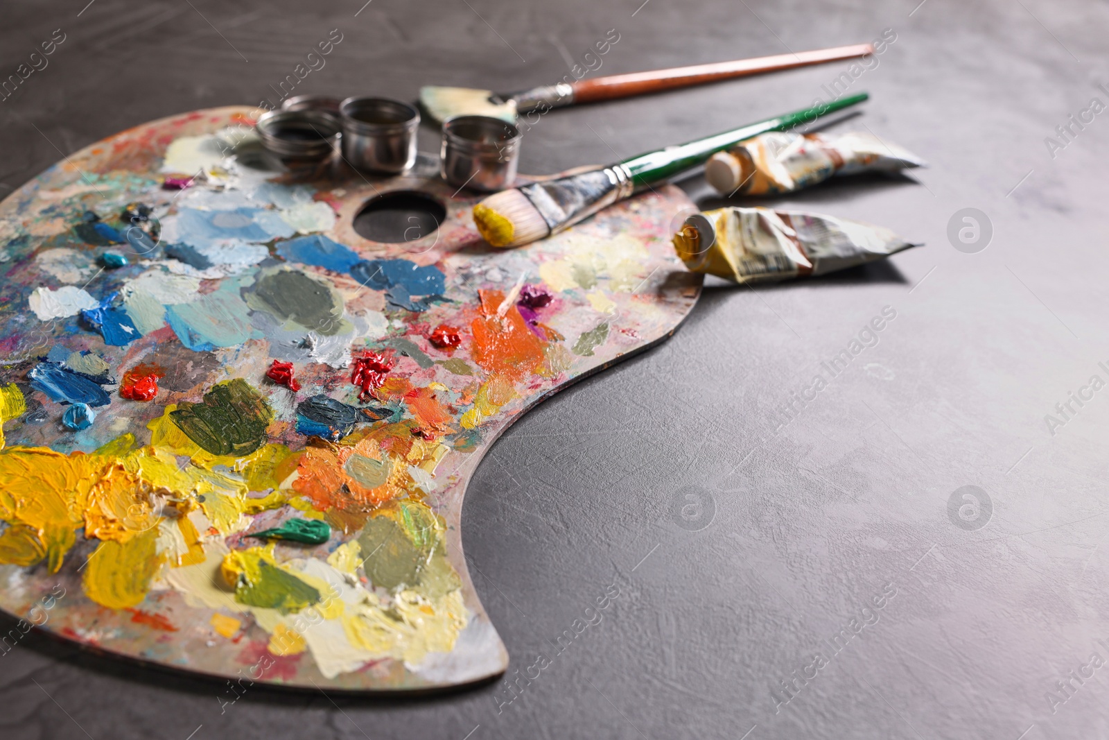 Photo of Artist's palette, brushes and paints on grey table, closeup. Space for text