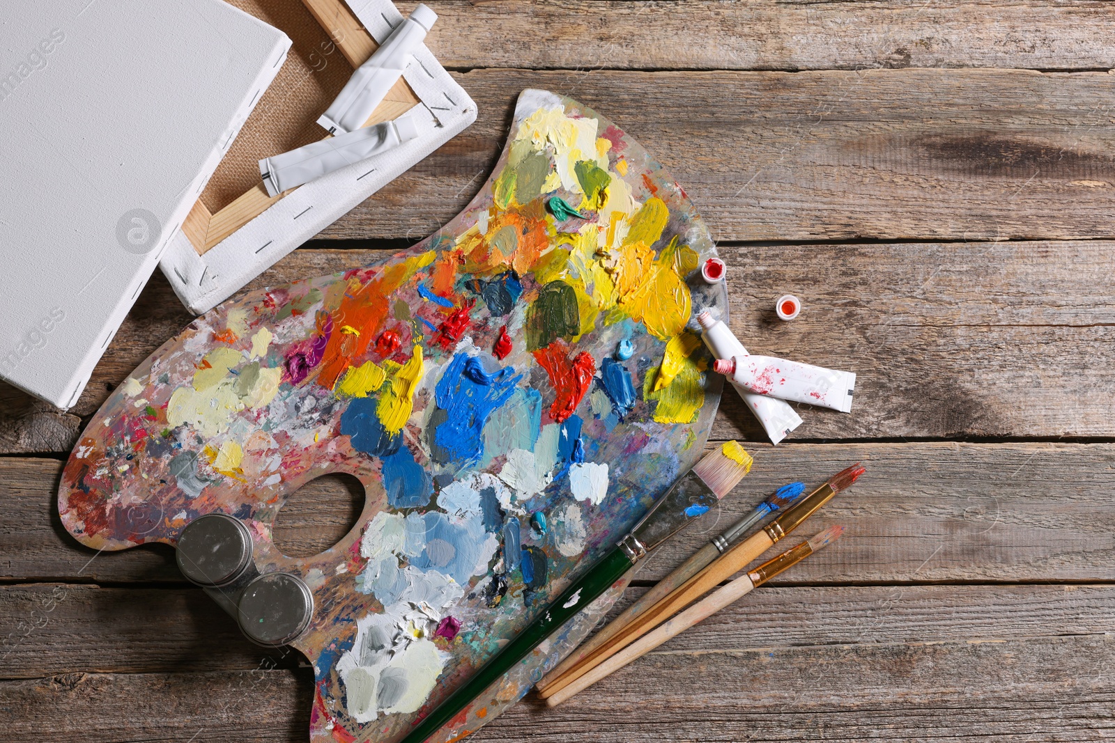 Photo of Artist's palette, brushes, paints and blank canvases on wooden table, flat lay