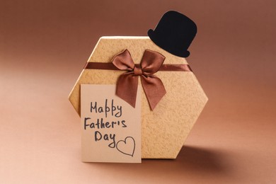 Card with phrase Happy Father's Day, hat and gift box on light brown background