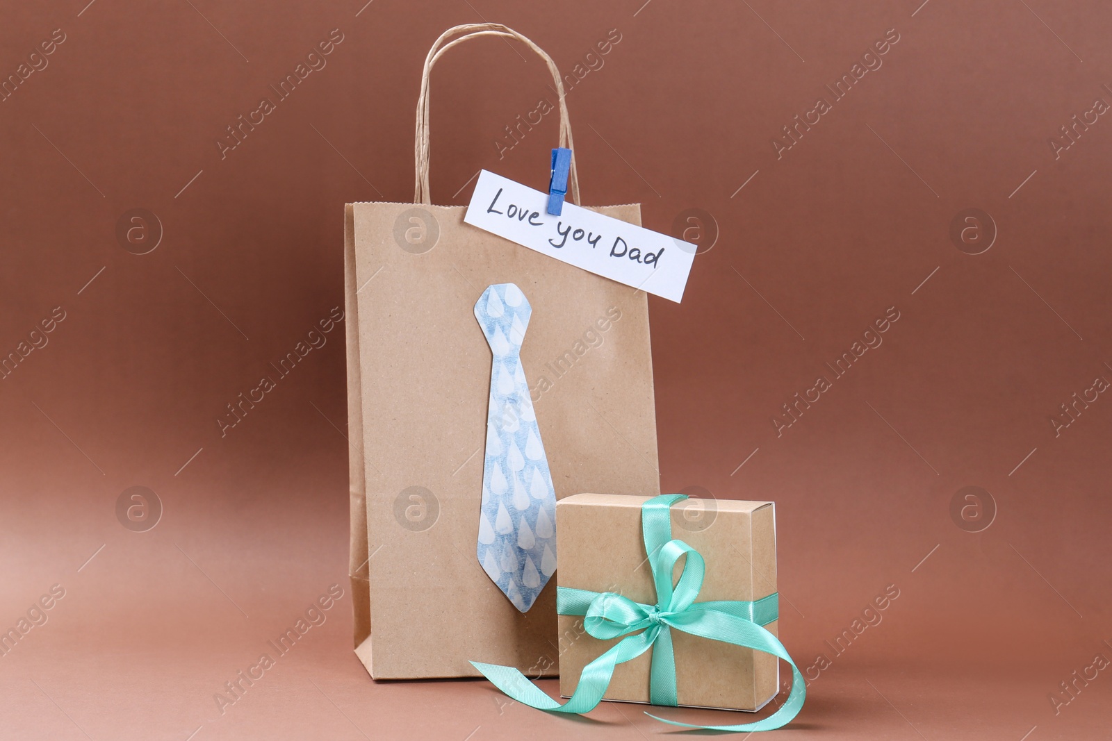 Photo of Happy Father's Day. Paper bag with tie, phrase Love You Dad and gift box on light brown background