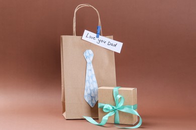 Photo of Happy Father's Day. Paper bag with tie, phrase Love You Dad and gift box on light brown background