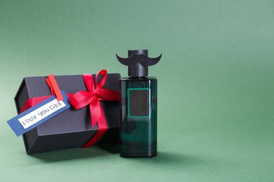 Photo of Happy Father's Day. Bottle of product with moustache, phrase Love You Dad and gift box on green background, space for text