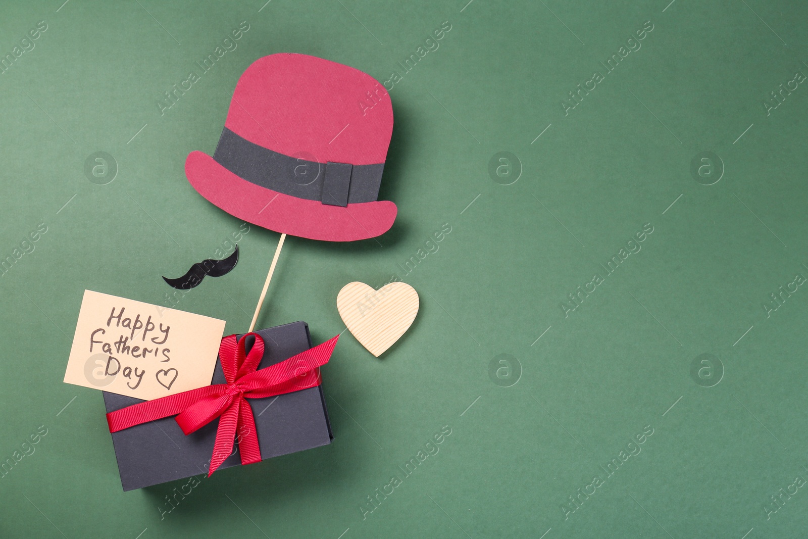 Photo of Card with phrase Happy Father's Day, gift box, heart, moustache and paper hat on green background, flat lay. Space for text